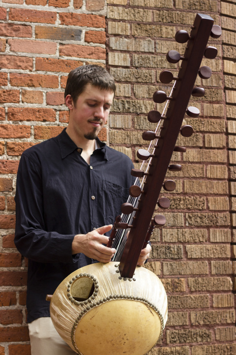 Photo of musician Sean Gaskell holding Kora and standing in front of brick wall