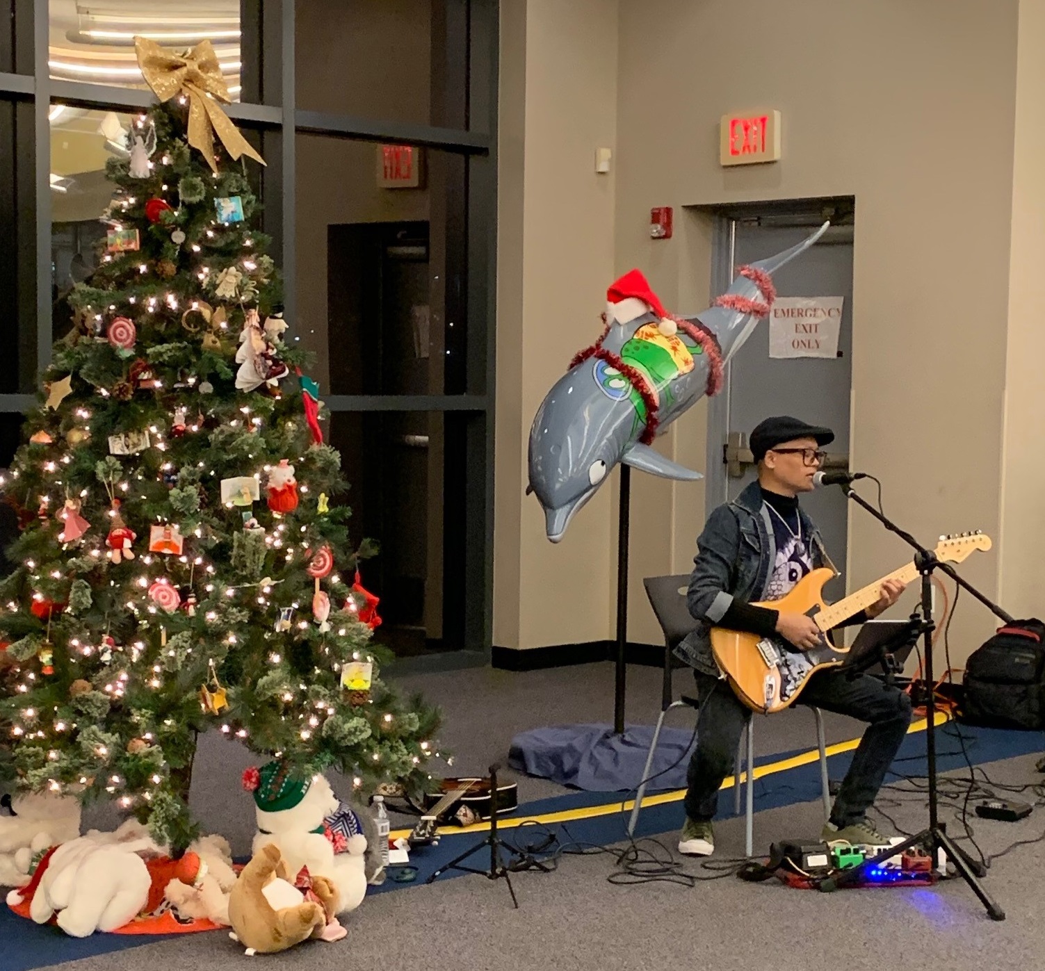 Photo of Ashesh Dangol playing guitar near decorated Christmas tree